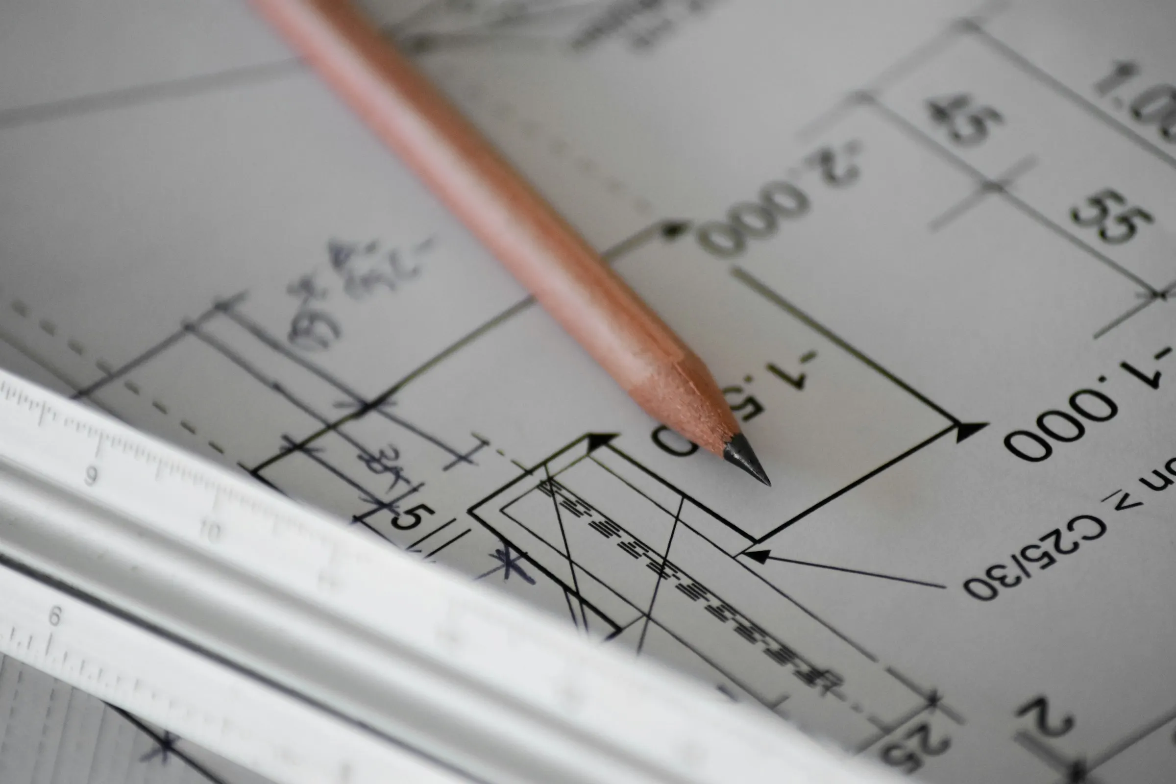 A pencil resting on a dimensioned technical drawing, a scale ruler beside it.